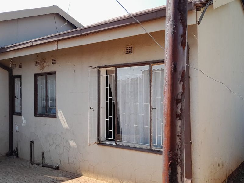 Rear exterior view of the property featuring paved courtyard area, security bars on windows, and weathered plaster finish requiring maintenance.