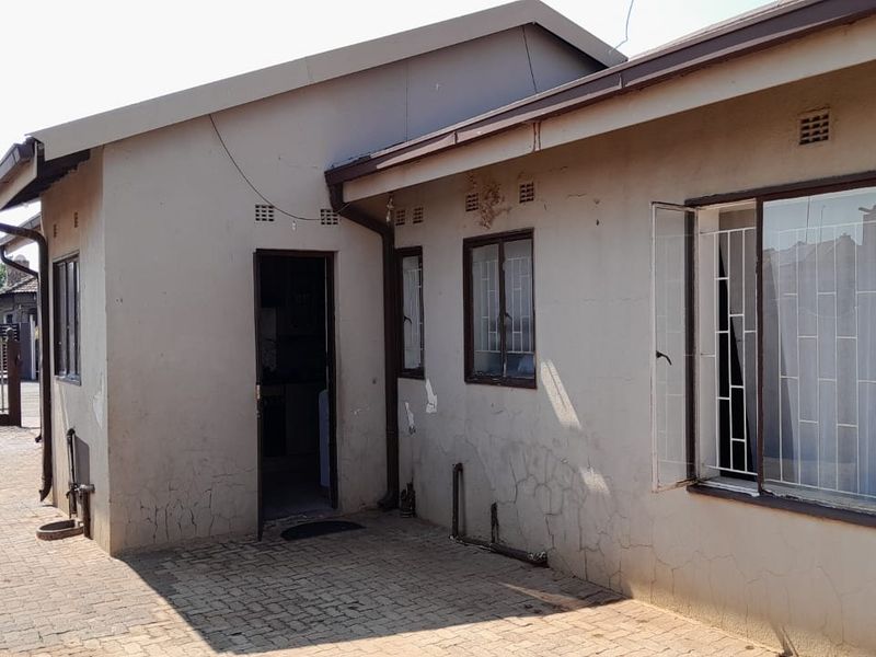Rear exterior view of the house featuring paved ground, metal security bars on windows, and visible wear to the exterior wall plaster and paint.