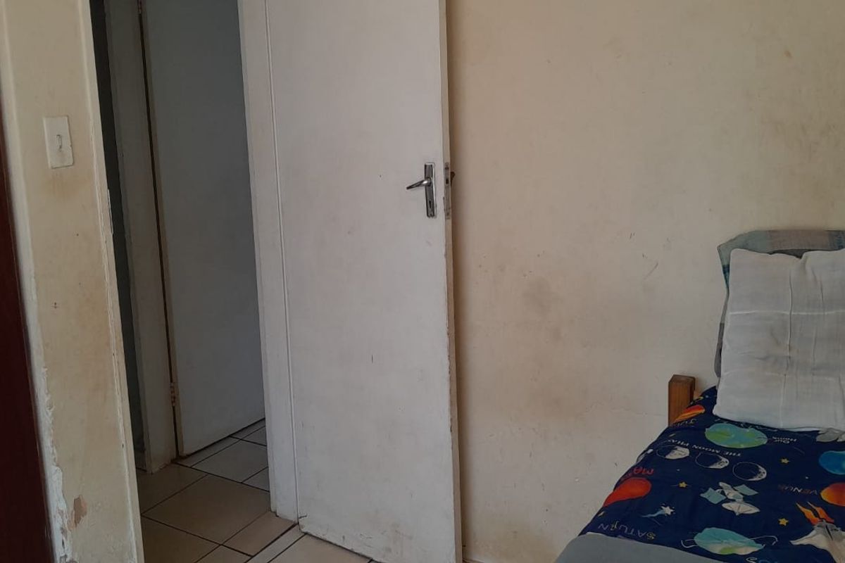 A bedroom interior featuring tiled flooring and internal door access, currently showing significant wear and staining on the wall surfaces.