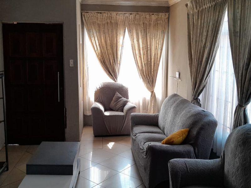A living room featuring tiled flooring, large windows with curtains, and a solid wood entrance door.