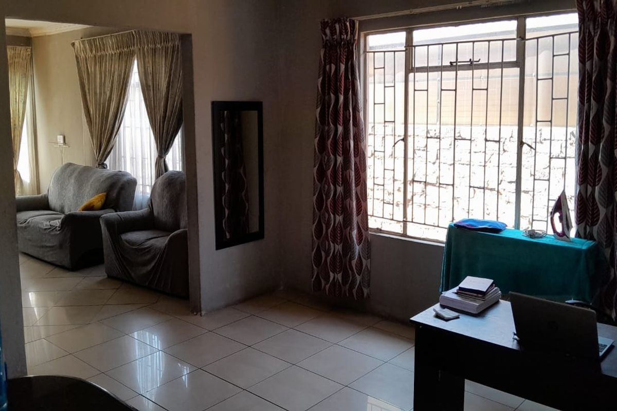 A living area featuring tiled flooring and large windows with security bars, offering a functional space with potential for modern updates.