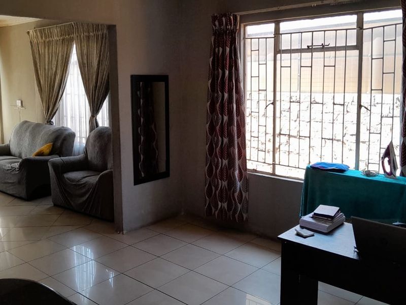 A living area featuring tiled flooring and large windows with security bars, offering a functional space with potential for modern updates.