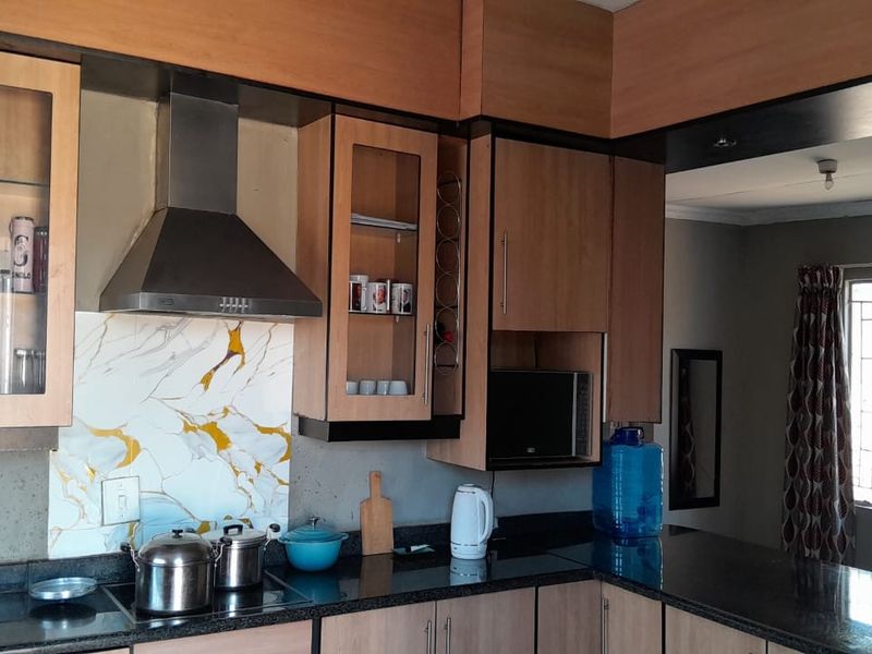 A functional kitchen featuring wood-finish cabinetry, granite countertops, a modern extractor fan, and a decorative marble-look splashback.