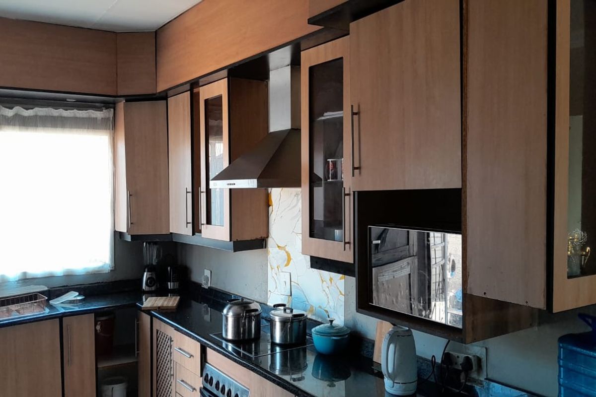 A functional kitchen featuring laminate cabinetry, granite countertops, a built-in oven, and a stainless steel extractor fan with a decorative glass splashback.