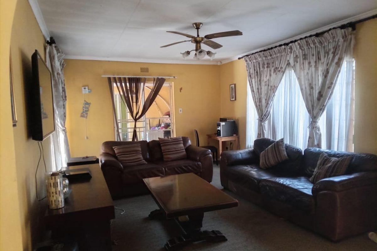 A spacious living room featuring a ceiling fan, large windows with curtain rails, and access to an outdoor area through a sliding door.