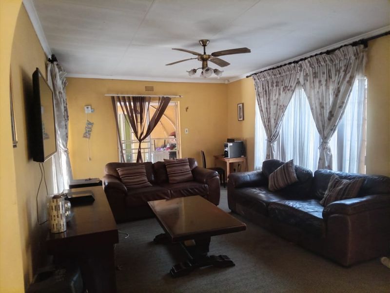 A spacious living room featuring a ceiling fan, large windows with curtain rails, and access to an outdoor area through a sliding door.