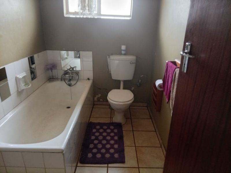 A functional bathroom featuring a standard bathtub, toilet, and tiled finishes, currently requiring cosmetic updates and repairs to the wall surfaces.