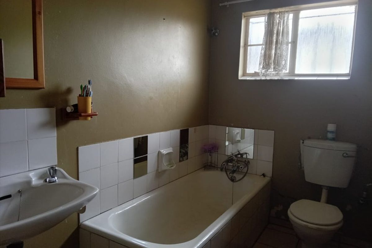 A functional bathroom featuring a bathtub, pedestal basin, and toilet, with tiled splashbacks and a window for natural light.