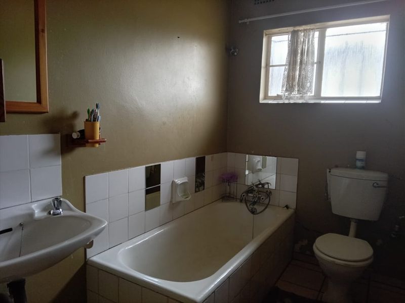 A functional bathroom featuring a bathtub, pedestal basin, and toilet, with tiled splashbacks and a window for natural light.