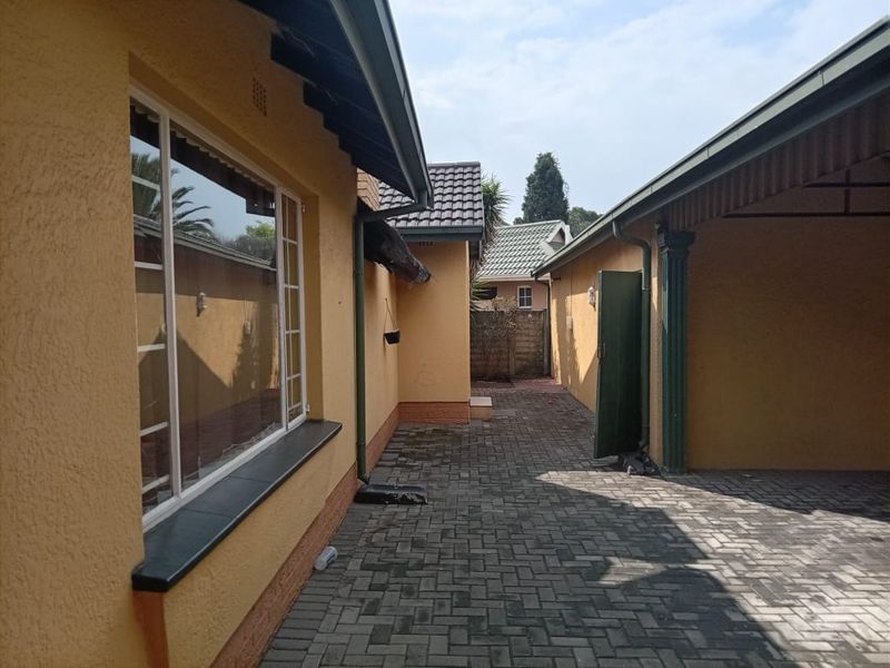 A side view of the property showing a paved walkway, covered carport area, and plastered exterior walls with tiled roofing.