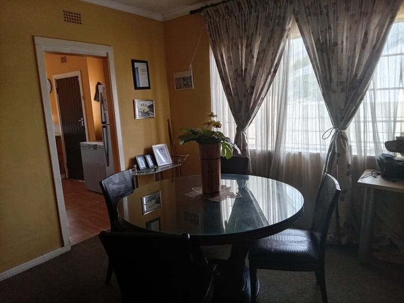 A dining room area featuring neutral wall finishes and natural light through a window, with an adjacent view into a secondary utility space.