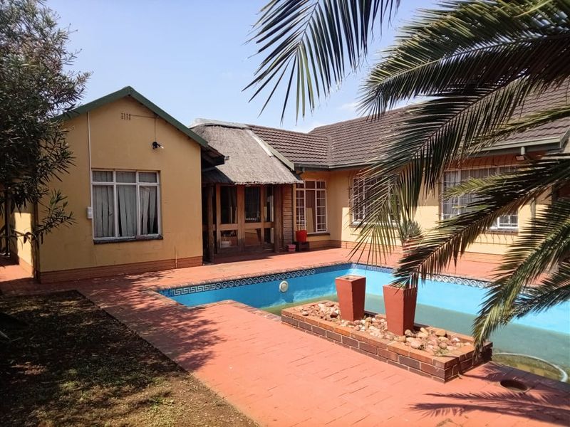 Rear exterior view featuring a swimming pool, brick paved patio area, and a combination of thatched and tiled roof sections.