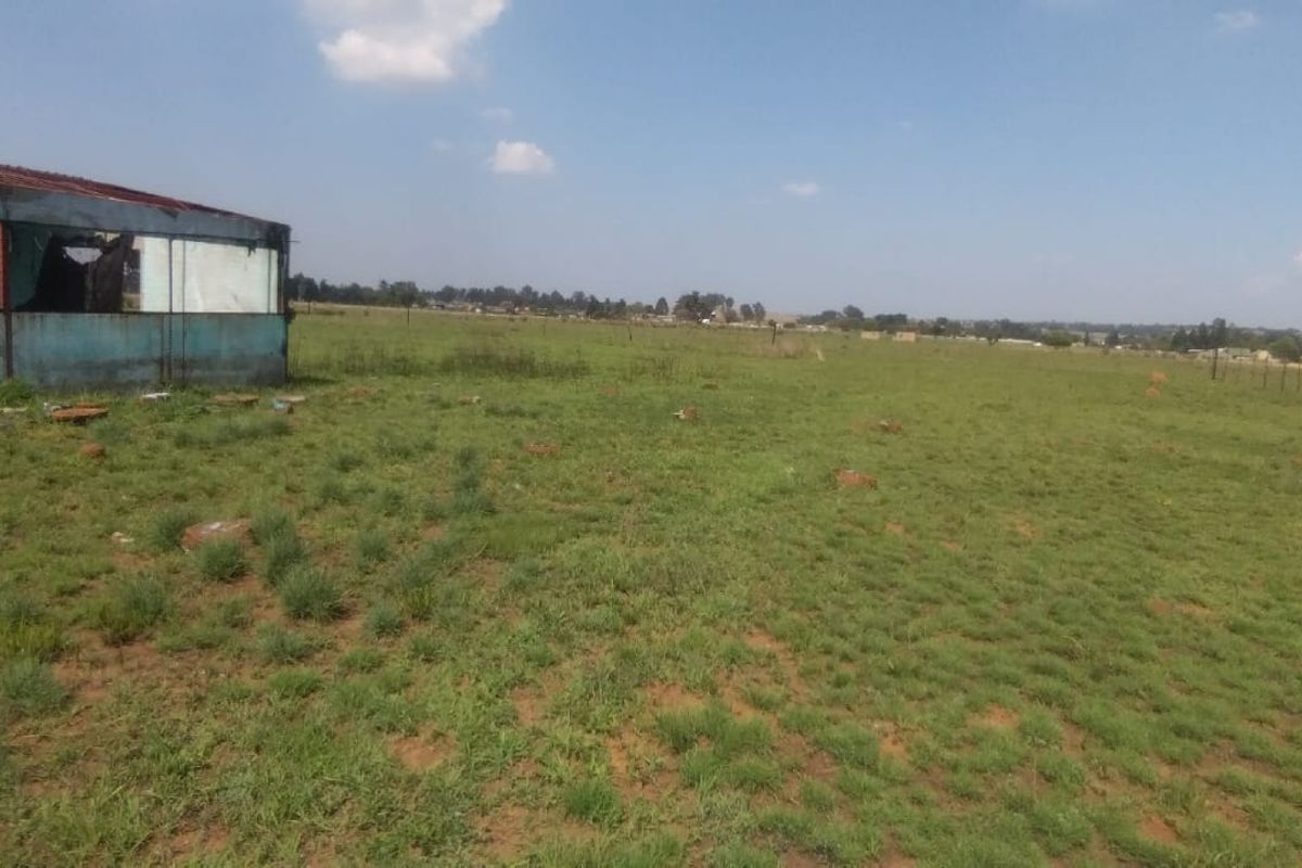 Expansive open land area featuring a dilapidated outbuilding structure and perimeter fencing.