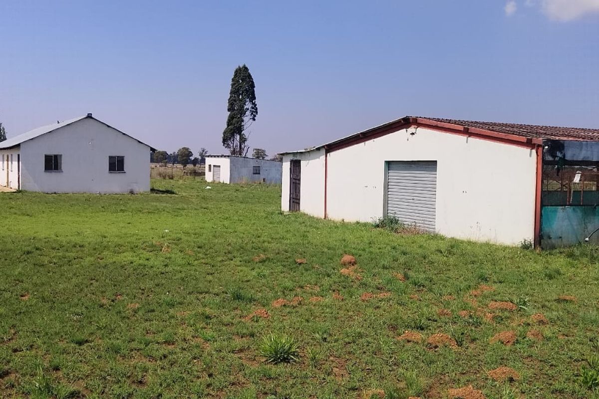 View of the property grounds featuring multiple outbuildings, including a structure with a metal roller door and corrugated roofing set on a large plot.