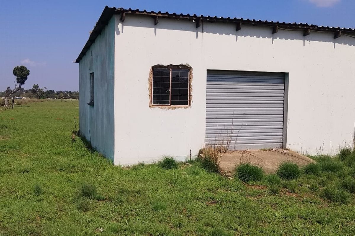 A detached single garage structure featuring a roller shutter door and metal window frame, situated on a large open plot.
