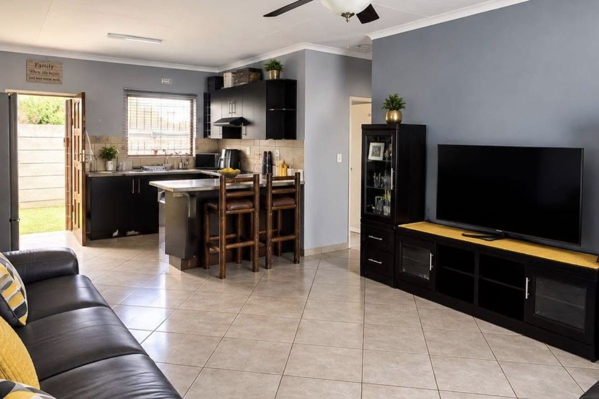 Open-plan living area featuring tiled floors, a ceiling fan, and a functional kitchen with dark cabinetry and a breakfast counter.