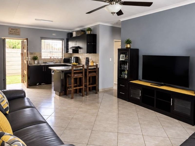 Open-plan living area featuring tiled floors, a ceiling fan, and a functional kitchen with dark cabinetry and a breakfast counter.