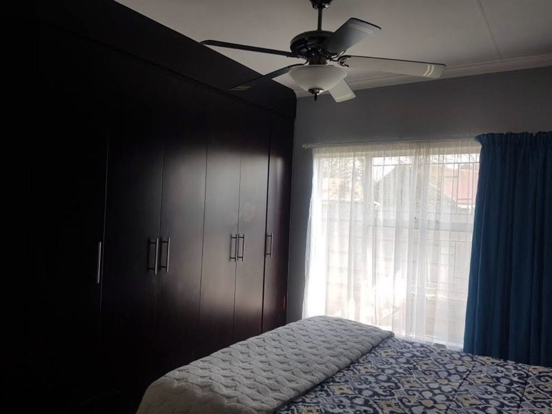 A bedroom featuring dark wood built-in cupboards, a ceiling fan, and windows fitted with security bars.
