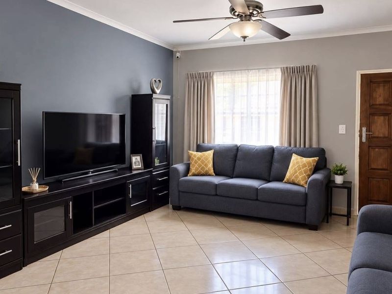 A well-maintained living room featuring neutral tiled flooring, a ceiling fan, and a feature wall, providing a comfortable and functional living space.