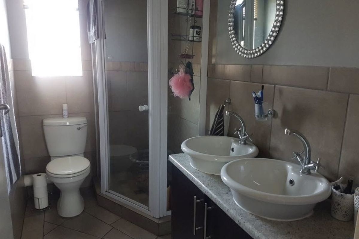 A functional bathroom featuring a double vanity with vessel sinks, a glass-enclosed shower, and a standard toilet with neutral wall and floor tiling.