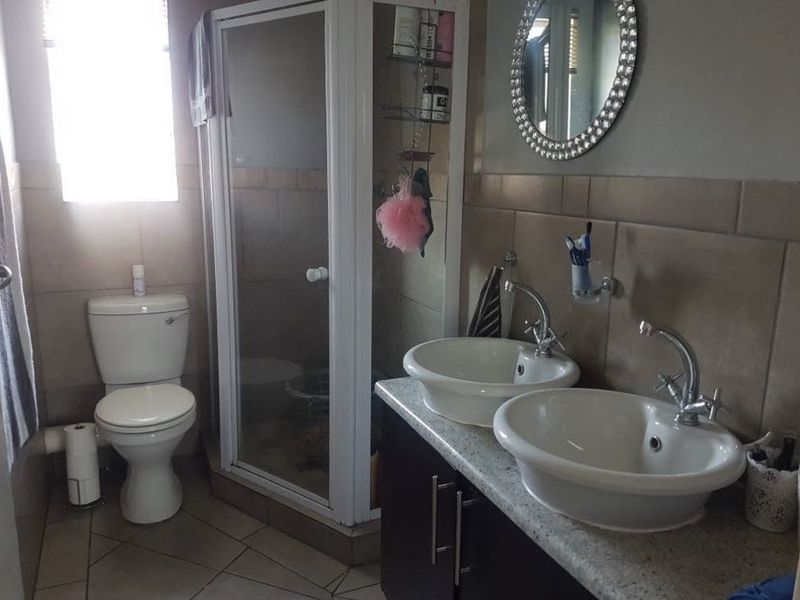 A functional bathroom featuring a double vanity with vessel sinks, a glass-enclosed shower, and a standard toilet with neutral wall and floor tiling.