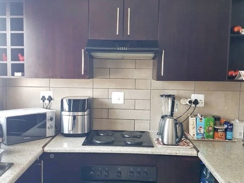 A functional kitchen featuring dark wood cabinetry, a subway tile backsplash, and integrated cooking appliances including an electric oven and hob.