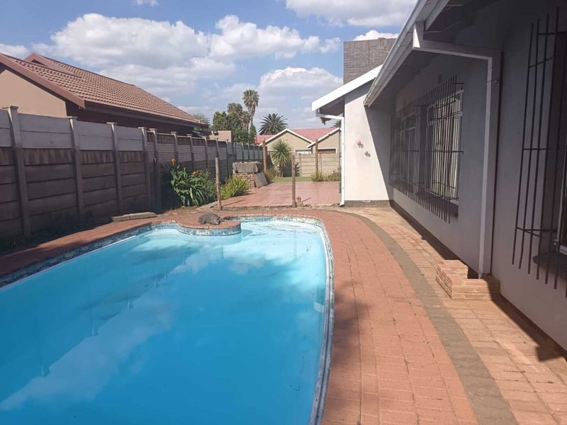 Rear garden area featuring a swimming pool with brick paved surround and secure boundary walling.