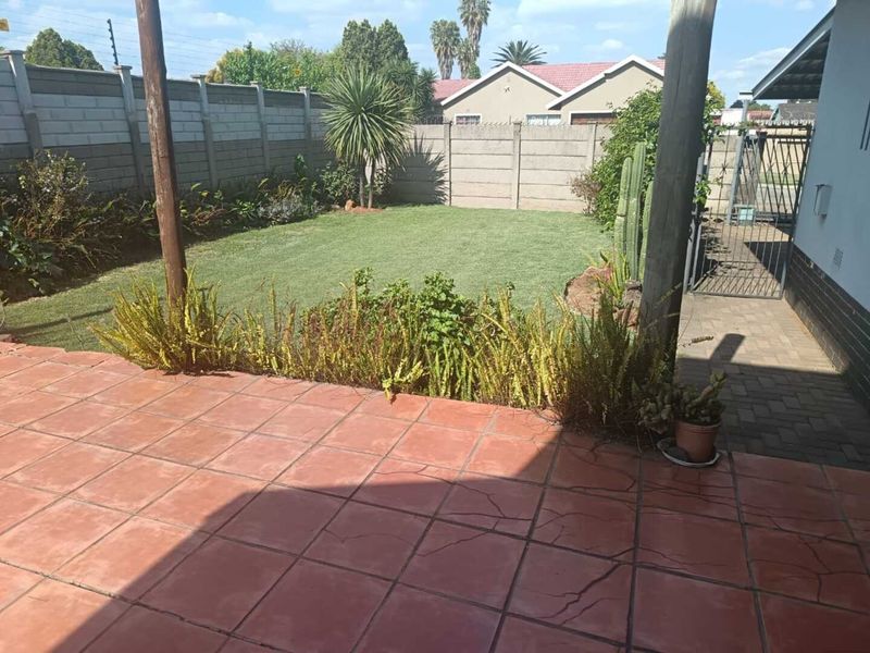 A rear garden area featuring a tiled patio with visible cracking, a well-maintained lawn, and secure perimeter walling.