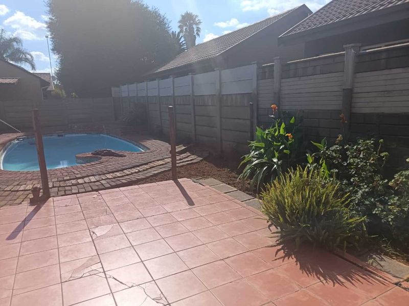 Outdoor area featuring a swimming pool with brick surround and a tiled patio space, enclosed by a precast concrete boundary wall.