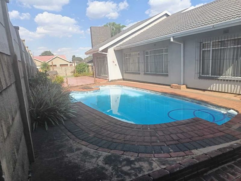 Rear garden area featuring a swimming pool with brick paving, surrounded by a precast concrete boundary wall and the rear elevation of the house.