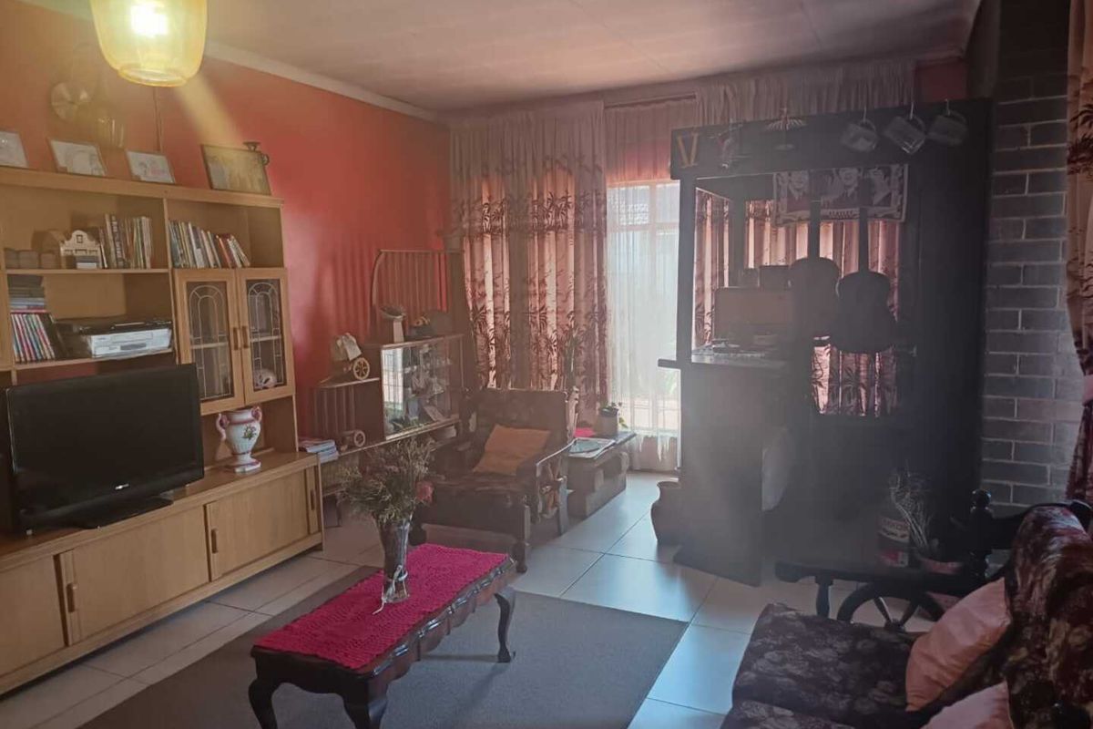 A living room featuring tiled flooring and a brick feature wall, currently presenting with dated finishes and worn paint.