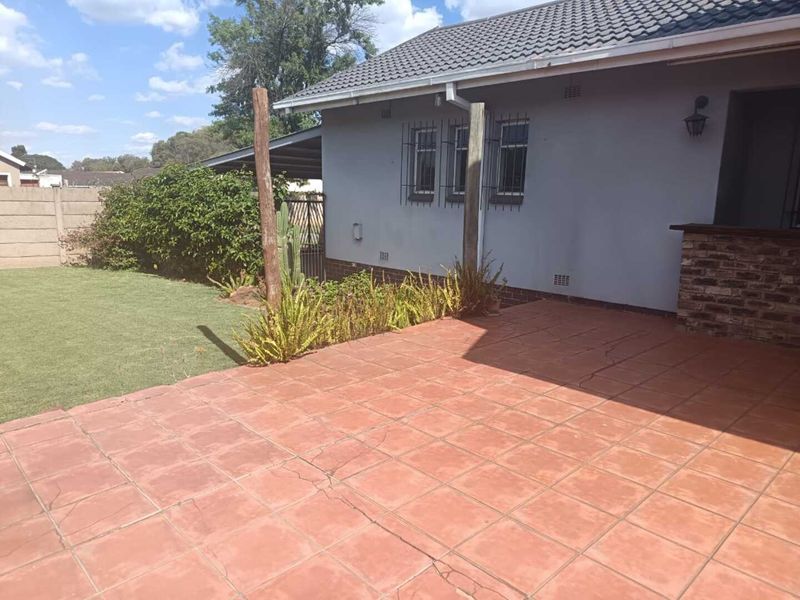 A paved outdoor patio area adjacent to the house, featuring brick accents and security bars on the windows.