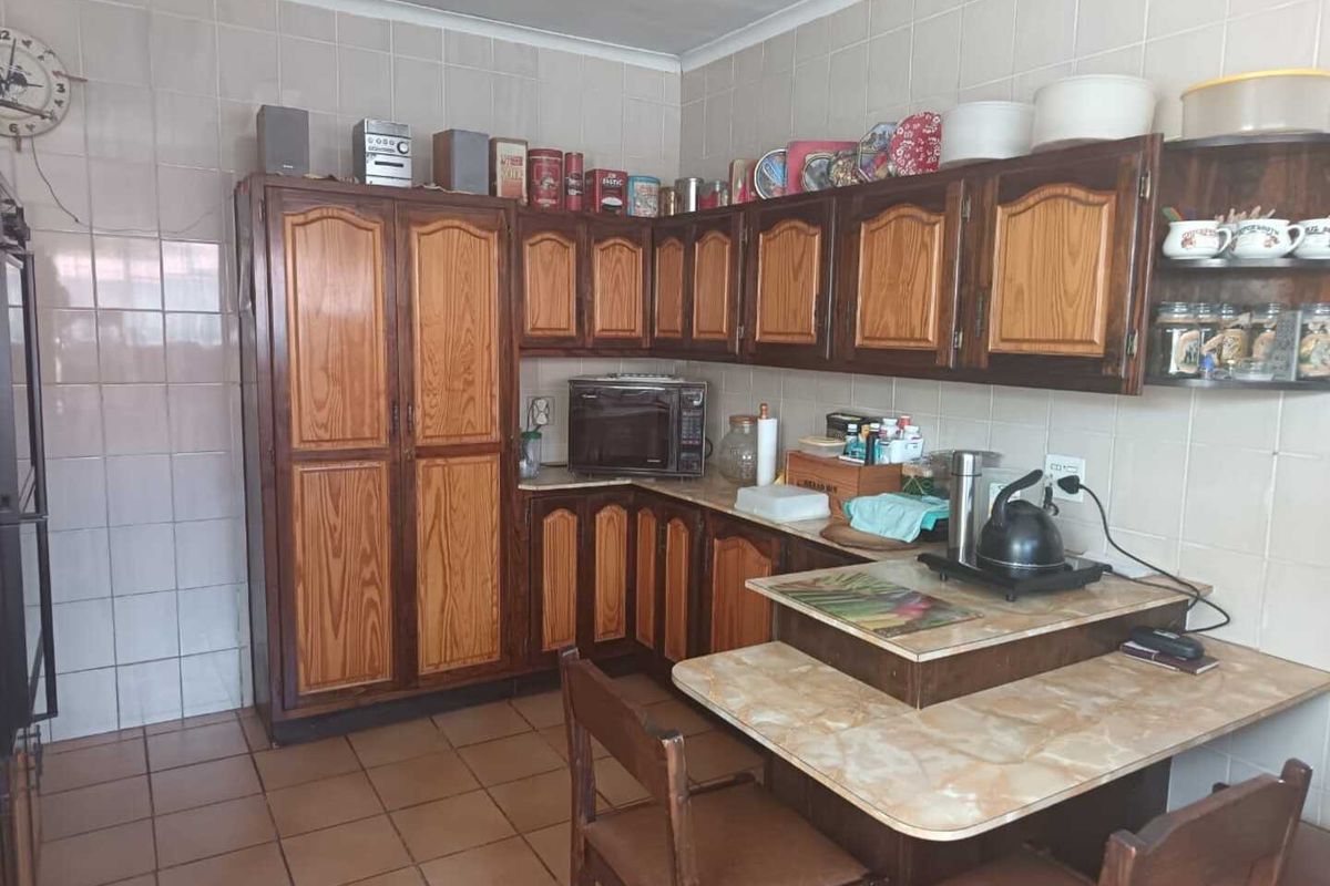 A functional kitchen featuring traditional wooden cabinetry, tiled walls, and tiled flooring, offering a classic layout with integrated storage and prep space.
