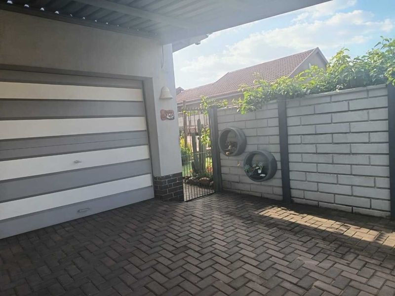 A neat front exterior view featuring a paved driveway, a modern garage door, and a secure boundary wall with a metal gate.