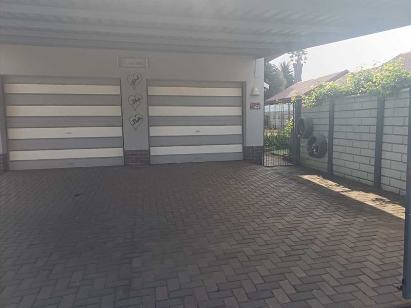 A double garage with a paved driveway and covered carport area, featuring a secure brick boundary wall and gated side access.