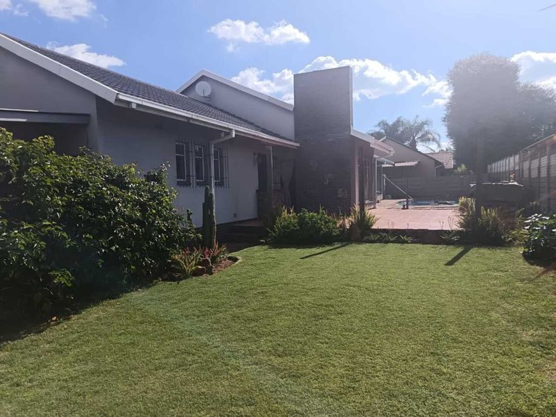 Rear view of the property featuring a well-maintained lawn, a paved patio area, and a swimming pool.
