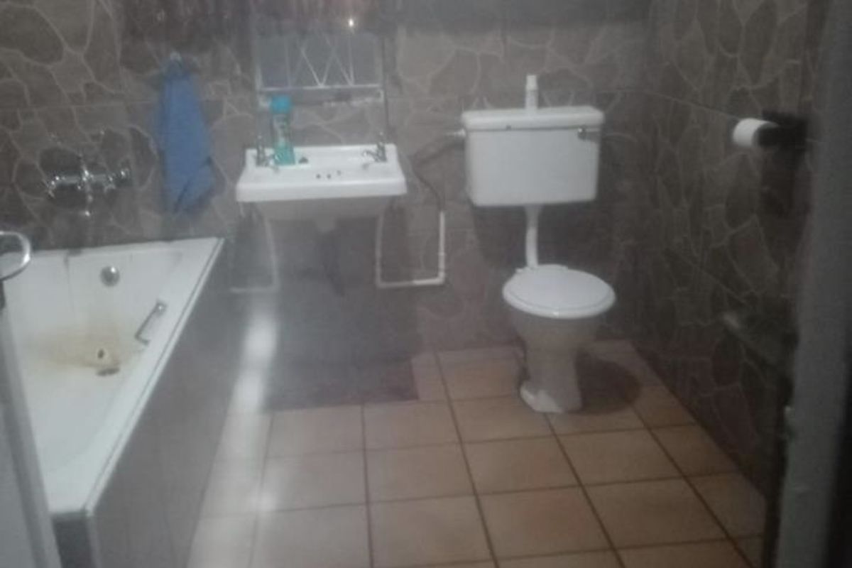 A dated bathroom featuring a bathtub, wall-mounted basin, and toilet with tiled walls and flooring, requiring cosmetic updates to improve its overall condition.