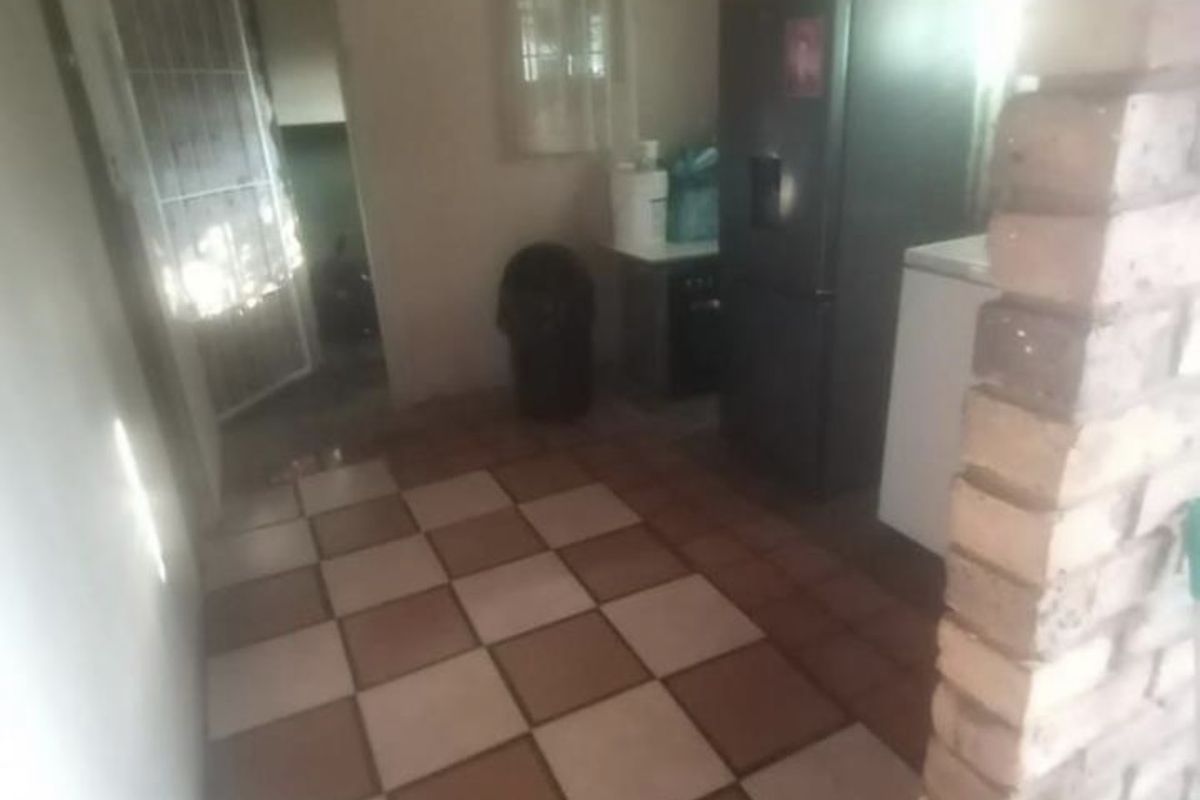 A functional kitchen area featuring a distinctive exposed brick pillar, timber ceiling, and checkered floor tiles, offering potential for modernization.