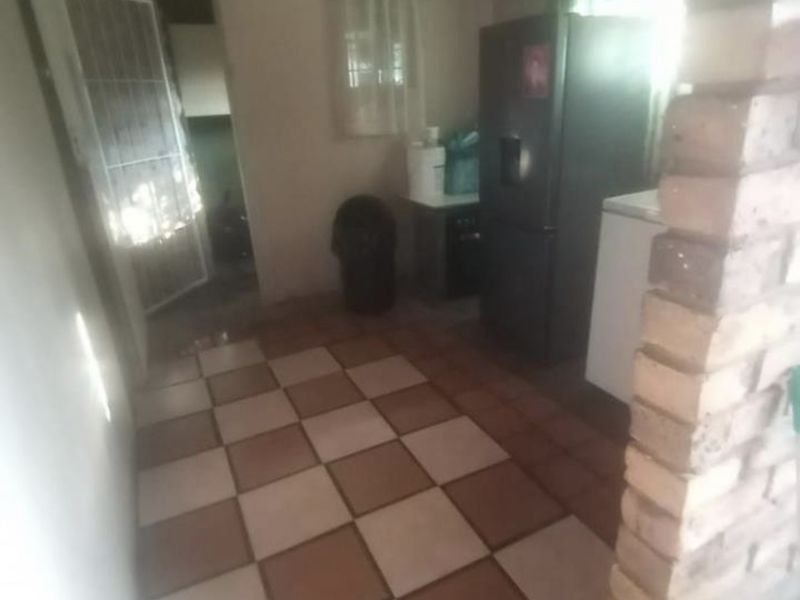 A functional kitchen area featuring a distinctive exposed brick pillar, timber ceiling, and checkered floor tiles, offering potential for modernization.