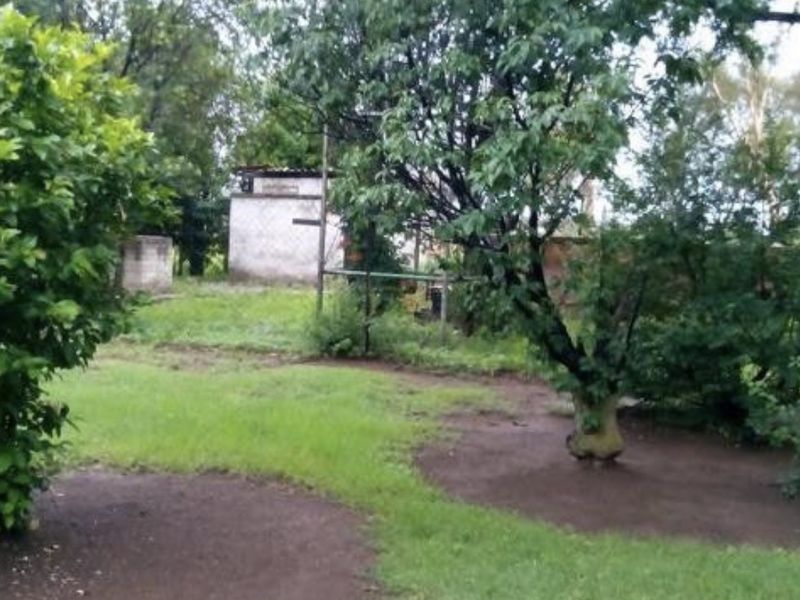 A spacious garden area featuring a lawn, mature trees, and a visible water tank structure in the background.