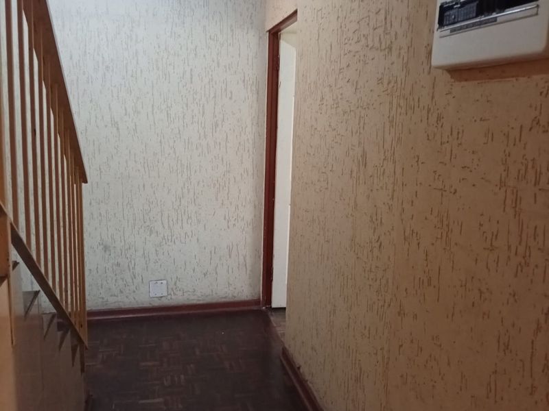 A functional hallway featuring parquet flooring, a wooden staircase with balustrade, and a wall-mounted electrical distribution board.