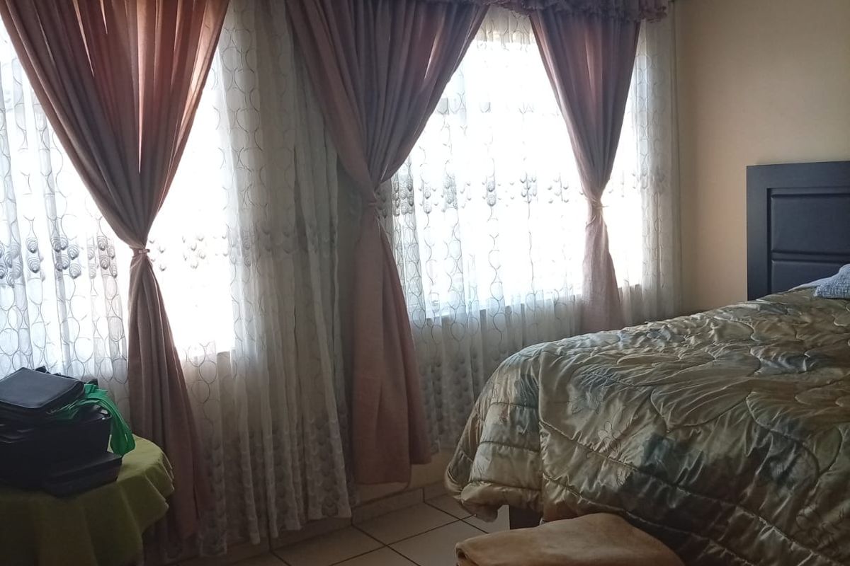 A bedroom featuring tiled flooring and a ceiling fan, with large windows allowing for natural light.