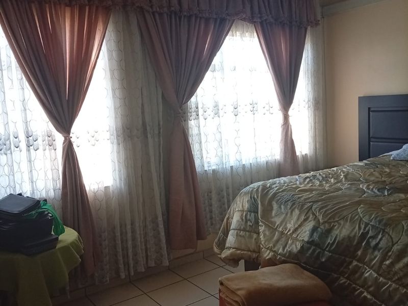 A bedroom featuring tiled flooring and a ceiling fan, with large windows allowing for natural light.