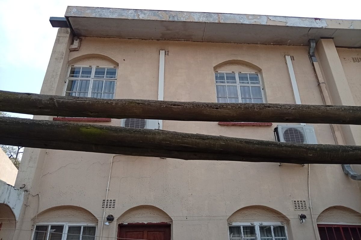 Rear exterior view of the apartment building featuring arched windows, mounted air conditioning units, and weathered timber pergola beams.