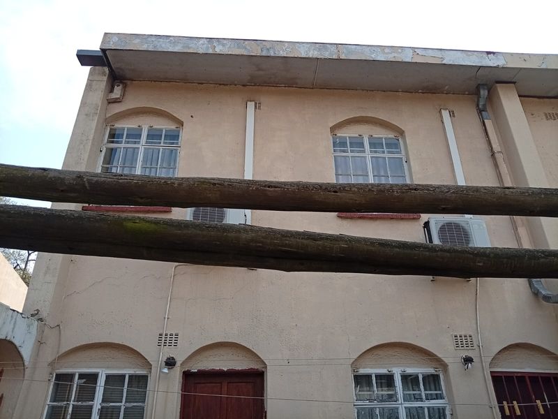 Rear exterior view of the apartment building featuring arched windows, mounted air conditioning units, and weathered timber pergola beams.