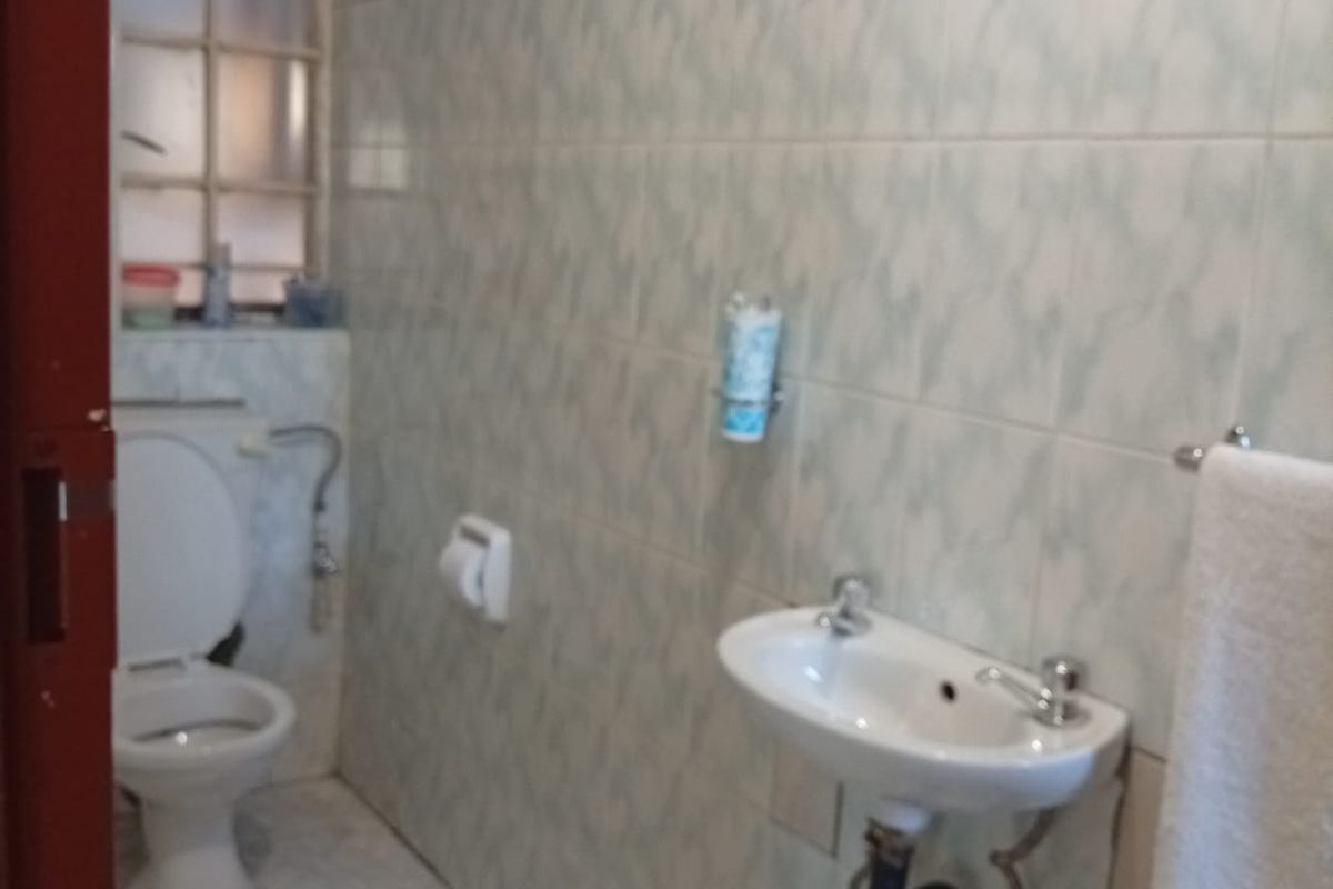 A functional bathroom featuring a wall-mounted basin, toilet, and full-height ceramic wall tiling. The space is ready for modernization.