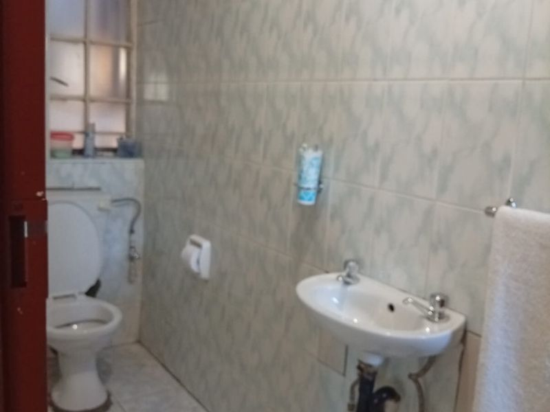 A functional bathroom featuring a wall-mounted basin, toilet, and full-height ceramic wall tiling. The space is ready for modernization.