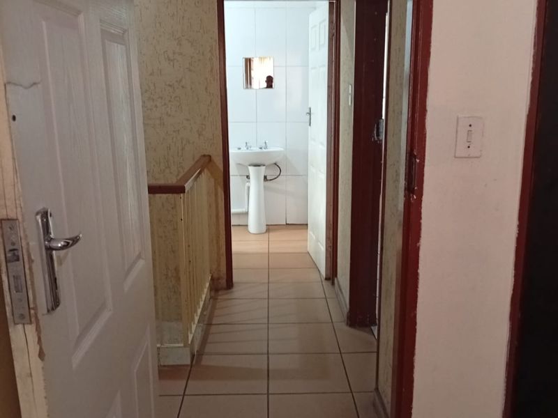 A view through a hallway featuring tiled flooring and textured walls, leading towards a bathroom area with a pedestal basin.