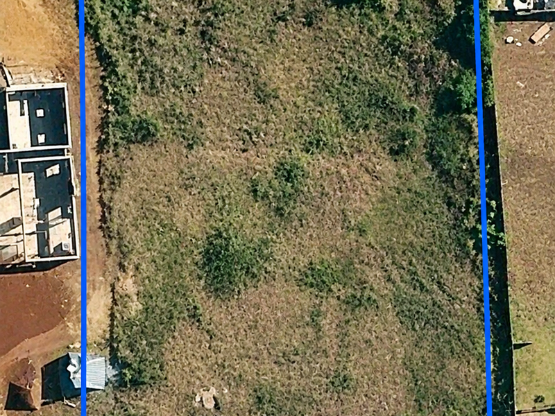 An aerial view of a vacant residential plot featuring natural vegetation and boundary fencing, ready for development.