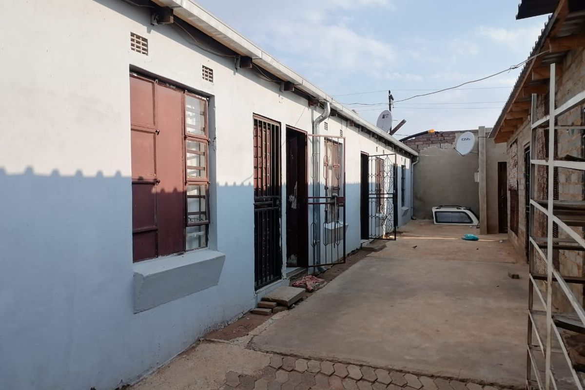 Rear exterior view of the apartment building featuring concrete paving, security gates, and steel window frames along the walkway.
